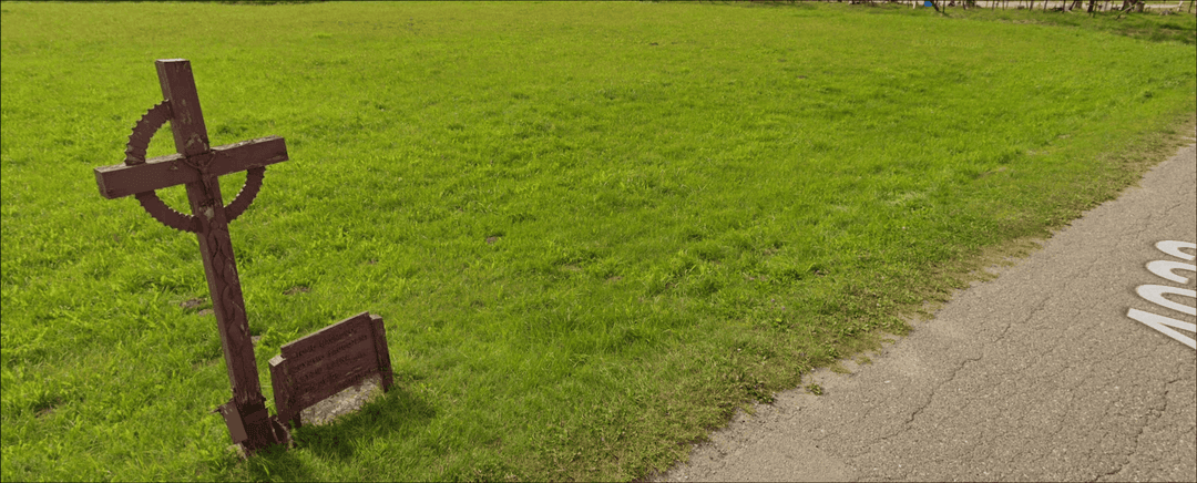 The challenge image, a wooden cross in a big grass field next to a road